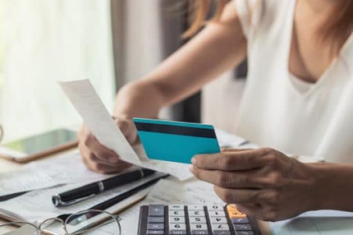 Person holding a credit card and utility bill sits at a desk with a calculator and a notebook.