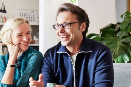 Happy couple laughing together in the kitchen. The man holds a small cup in his hand.