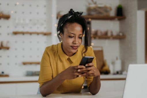 Woman in a modern kitchen uses her smartphone and laptop.