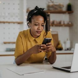 Woman in a modern kitchen uses her smartphone and laptop.