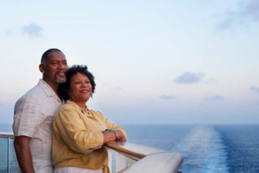 A man and woman stand together peacefully on the deck of a cruise ship admiring the sunset.