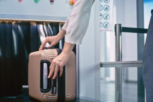 A person places their luggage on the conveyor belt of a TSA bag scanner.