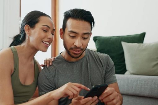 A woman explains length of credit history to her partner as they look at his credit score on his phone.