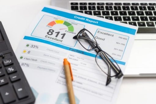 A credit report showing a person's credit rating sits next to a calculator and computer.
