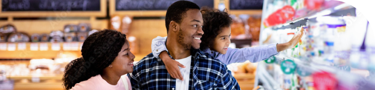A family shops together in a supermarket. A young child reaches for a product on a shelf.