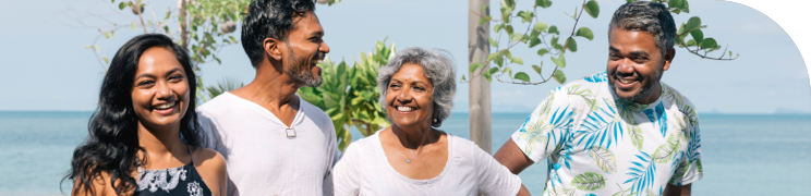 Four family members standing together outdoors, smiling and enjoying a sunny day by the ocean.
