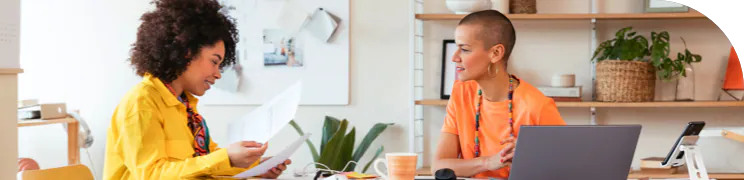 Two women sitting at a desk in an office, discussing documents