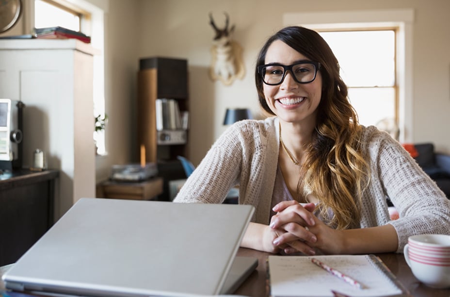 A woman smiling with a laptop partially closed on the table in front of her
