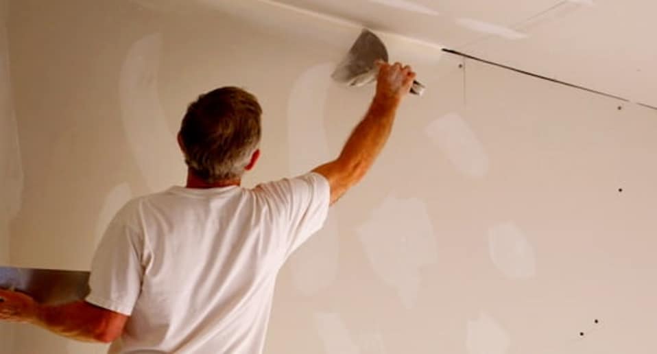 Image of man spreading drywall mud on wall