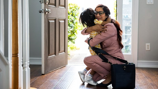 Woman crouching to hug child in front of an open door.