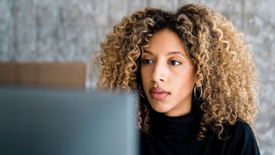 Young woman focuses as she looks at her laptop.