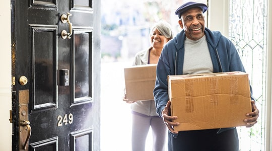 Two older adults smile move boxes into a home.