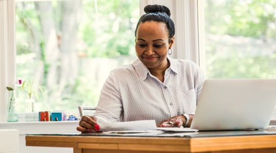 Smiling woman reviews paperwork at her desk.