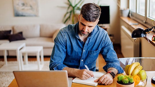 Man looking at computer and taking notes in a notebook.