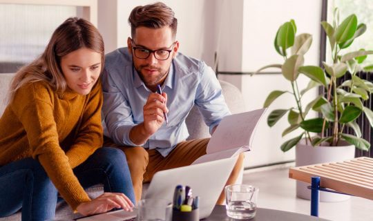 Man and woman sitting on a couch looking at a laptop together.