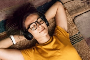 A person wearing headphones lying down with eyes closed and smiling