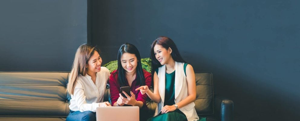 Three women look at a smartphone.