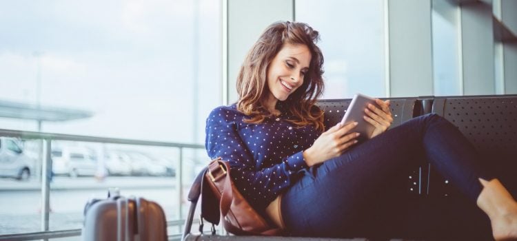 A woman sits on a bench and reviews her bank account on her tablet.