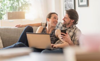 Couple looks at each other as they sit on the couch.