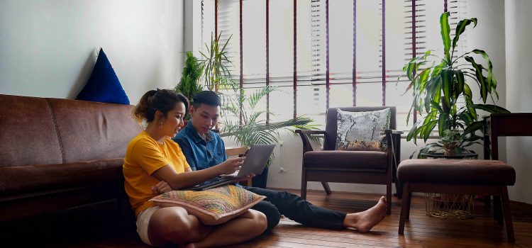 A man and a woman sit in the living room, reviewing their accounts on laptop computer.