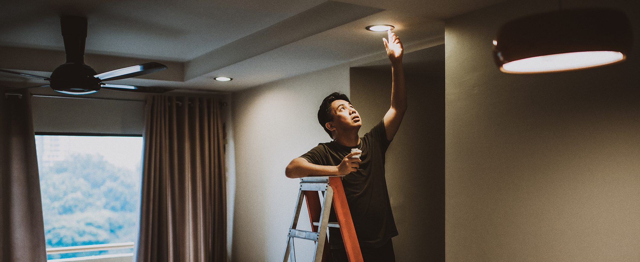 A man on a ladder adjusts a ceiling light bulb. 
