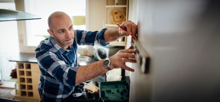 A man uses a level and a pencil to measure for a DIY installation in his home.