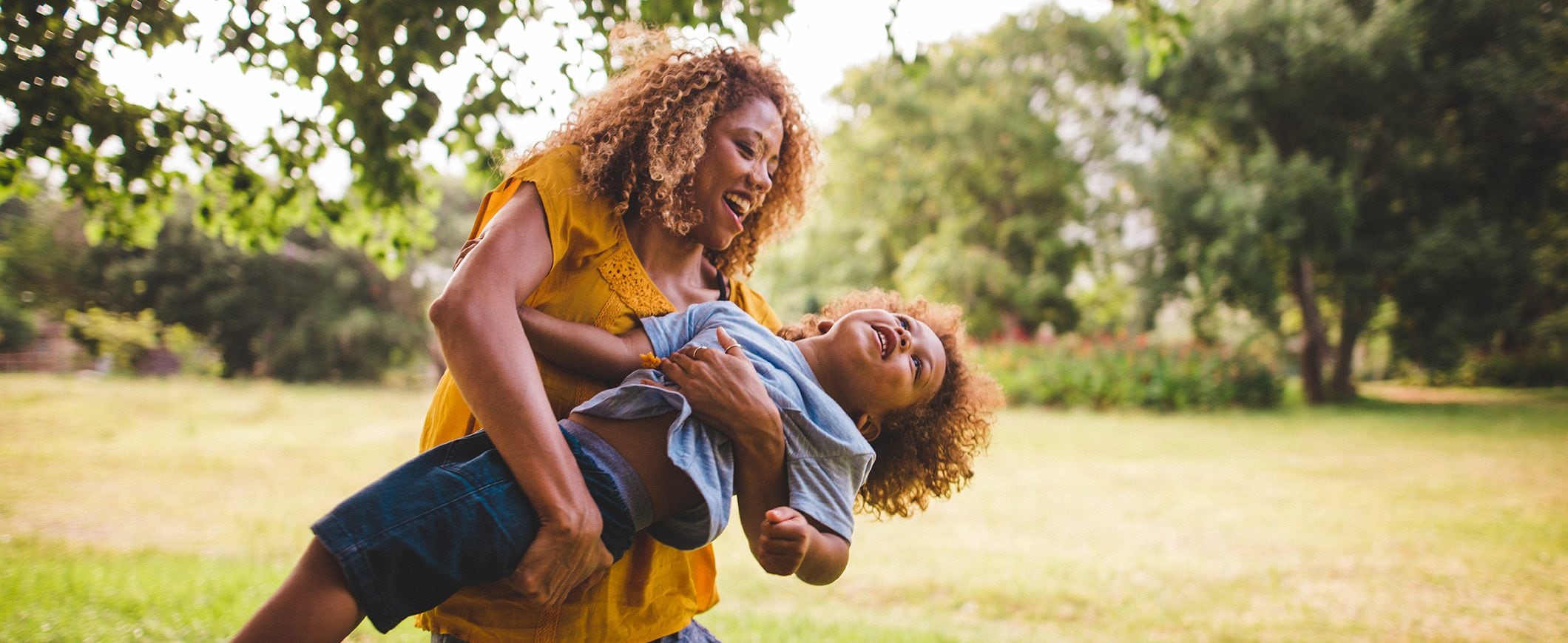 A woman holding her young child as they play in a grassy field.