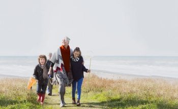 A young girl and boy walking with their grandma on the beach.