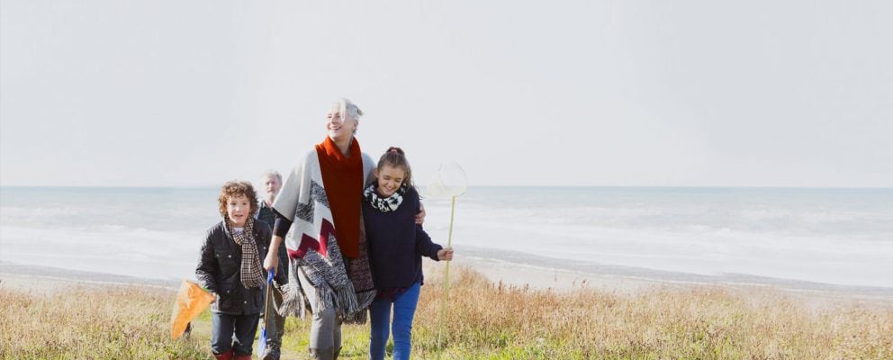 A young girl and boy walking with their grandma on the beach.