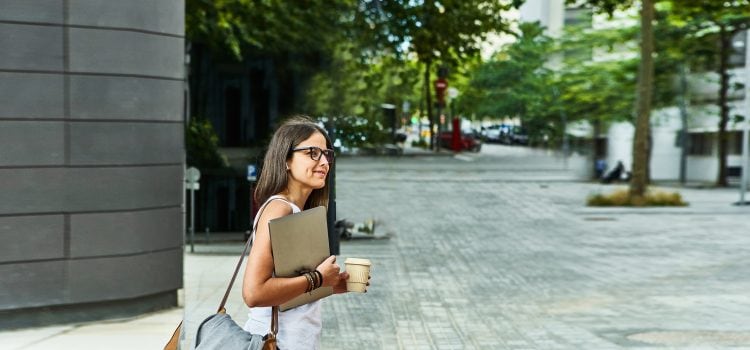 Woman carrying her laptop looks both ways before crossing the street.