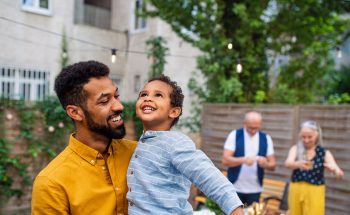 A father holds his son and smiles as they look up to the sky