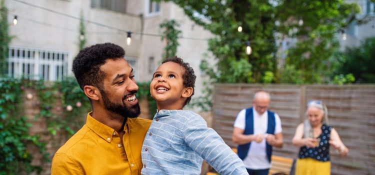 A father holds his son and smiles as they look up to the sky