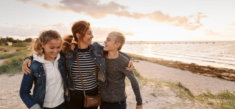 A mom and her two kids walk along the beach.