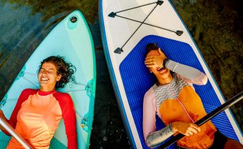 2 women on lie on paddle boards looking up and laughning