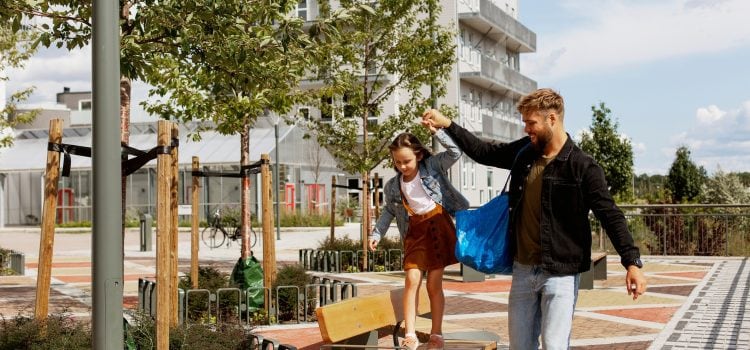 A father holds his daughters hand as she walks on a park bench.