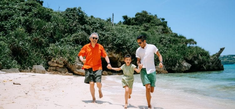 A family runs hand-in-hand along a beach on a sunny day.