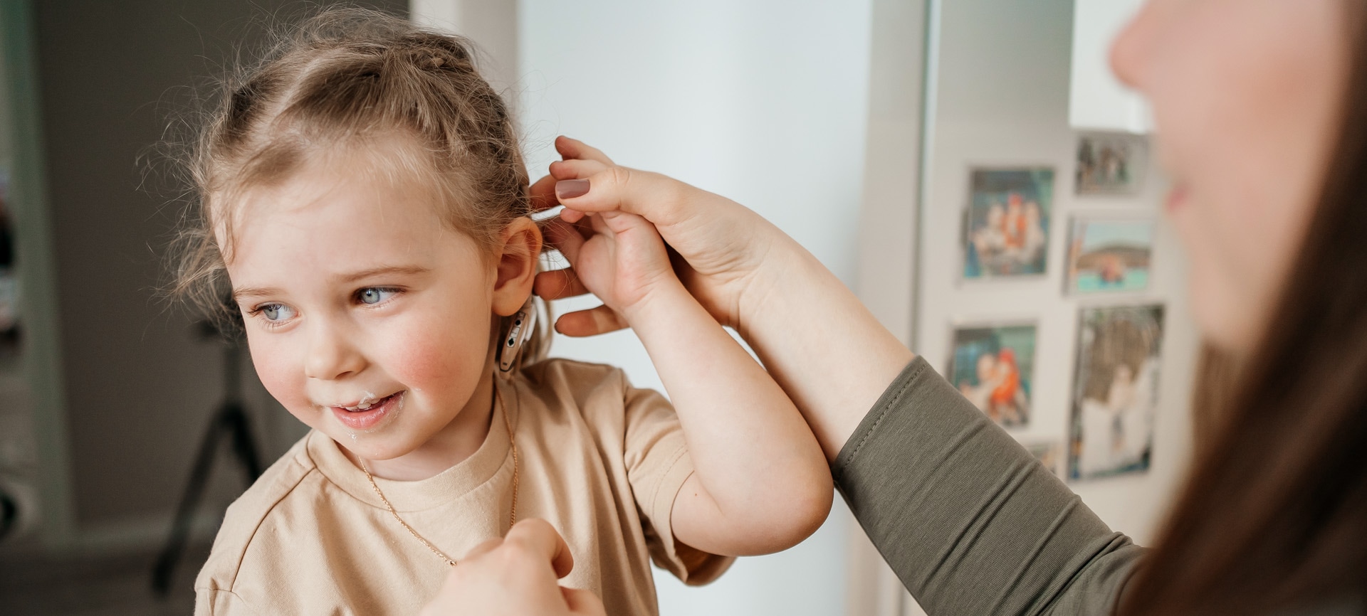 A young girl smiles while a woman, presumably her mother, gently tucks her hair behind her ear in a cozy indoor setting.