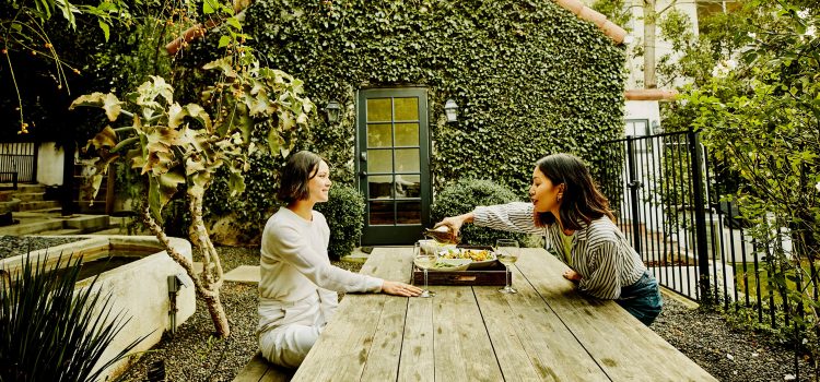 Two friends enjoy wine and salads at an outdoor garden table.