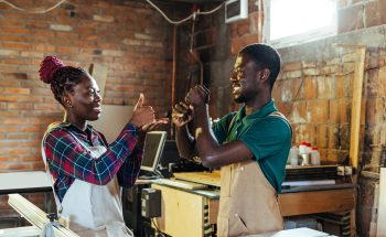 A man and woman use sign language in their workshop.