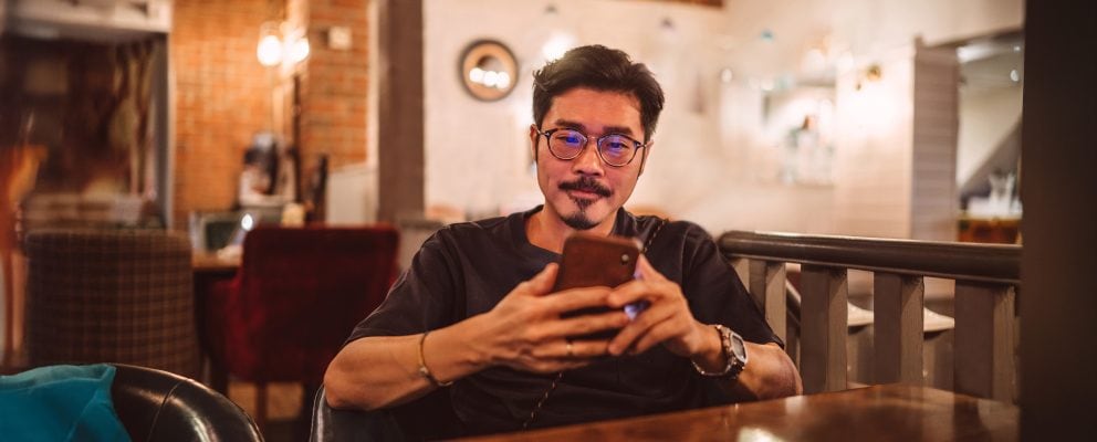 A young man sits and looks at his phone.