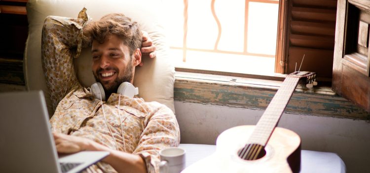 Man with headphones around his neck smiling at his computer.
