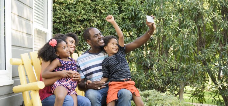 A mother and father with their son and daughter sitting on a bench outside.