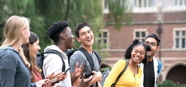 A group of college students laughing outside a campus building.