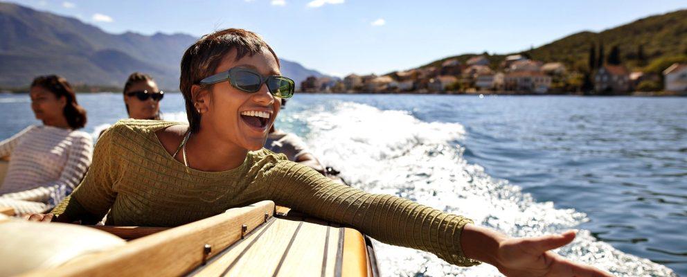A woman on a boat with 2 others extends her hand over the water with a big smile