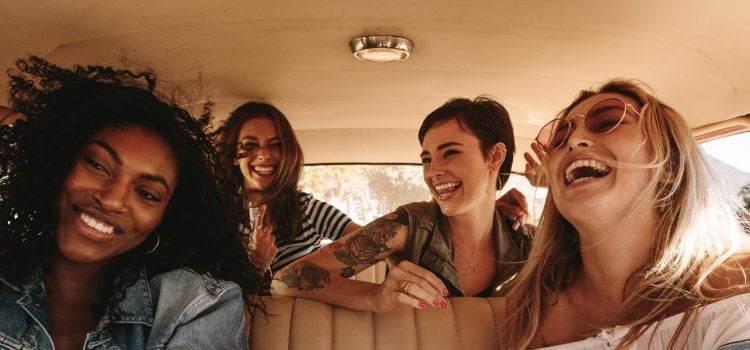 Four female friends smile and laugh during a road trip.