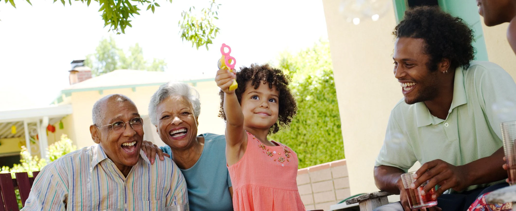 A little girl blows bubbles while her dad and grandparents adoringly look on.