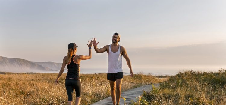 A man and a woman in workout gear high five in a field by the ocean.