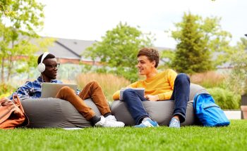 2 students lounge on bean bag chairs in the grass