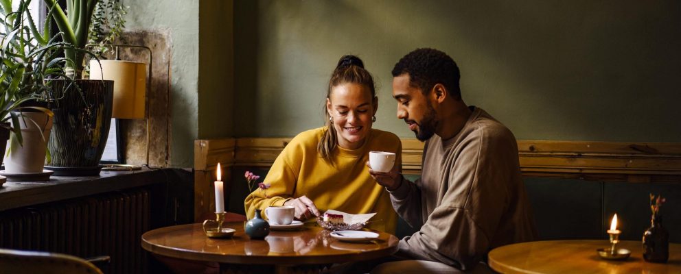 A couple at a café share a desert and drink coffee.