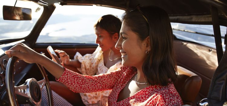 Woman driving a car while another woman sits in the passenger seat on her phone.